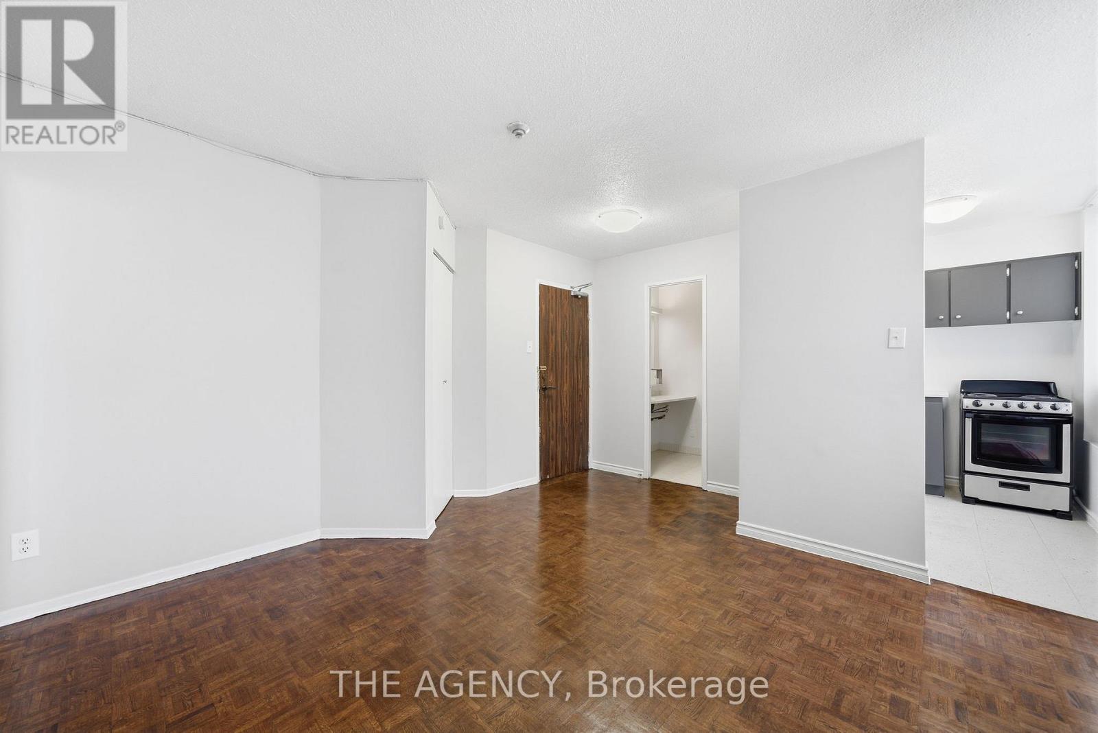 A spacious room with wood flooring and white walls, with a door in the middle and a stove on the right side.