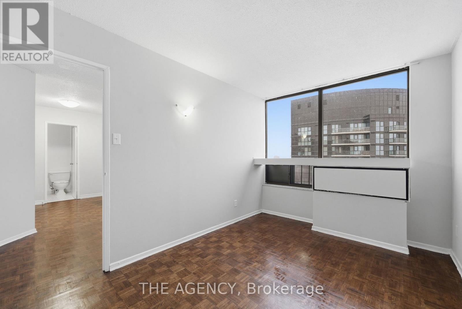 A room with a window overlooking a building with a sign that says "THE AGENCY, Brokerage".
