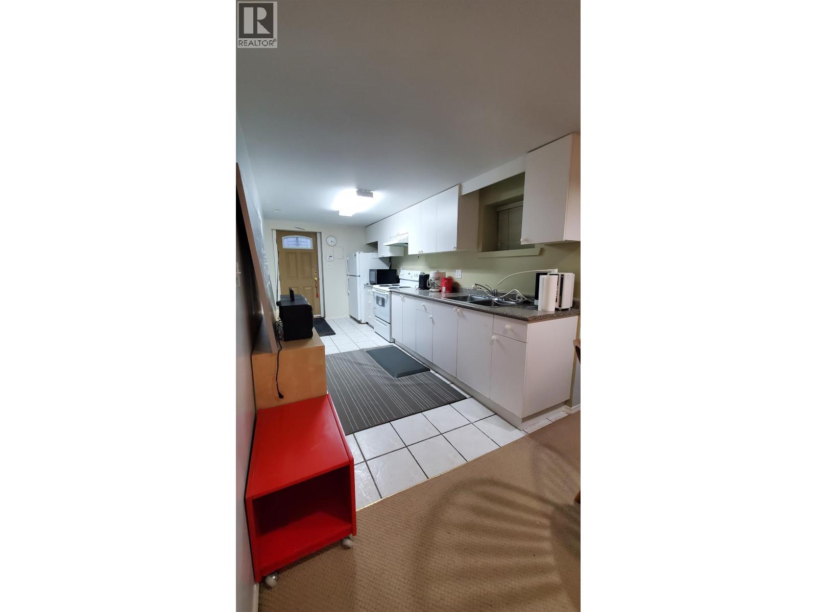 A kitchen with a red stool and white cabinets.