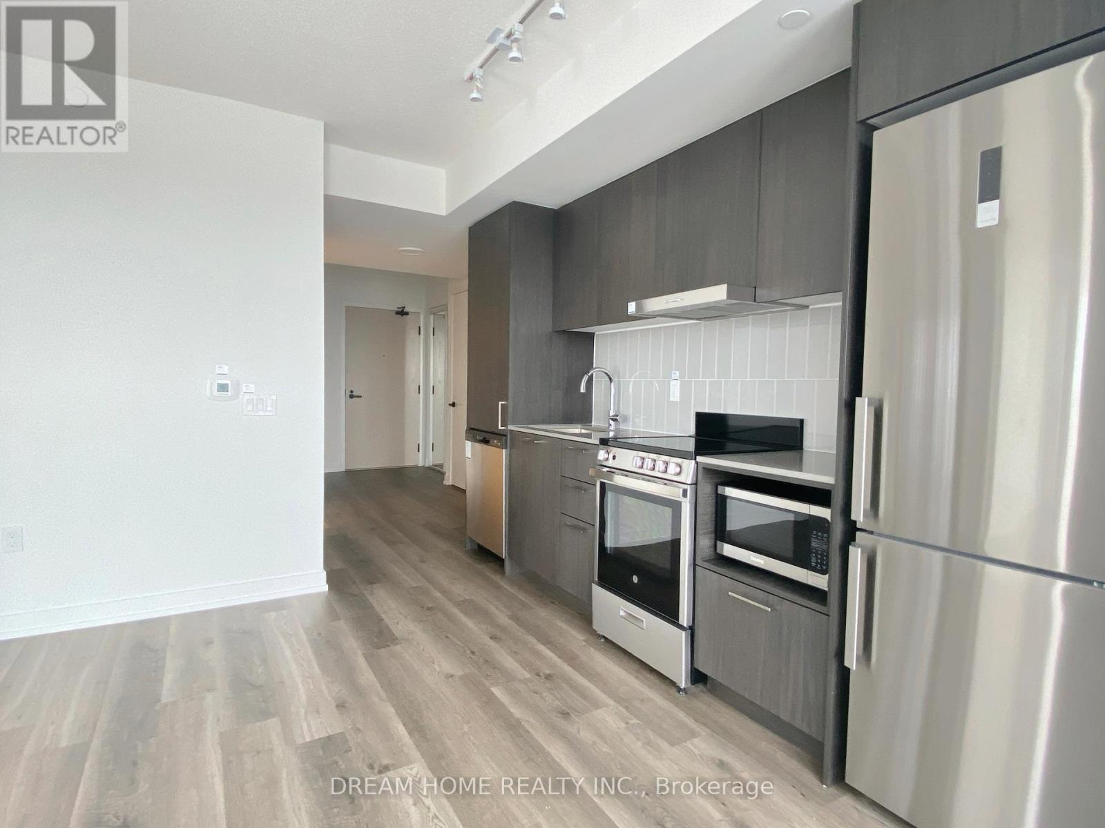 A modern kitchen with stainless steel appliances and wooden flooring.