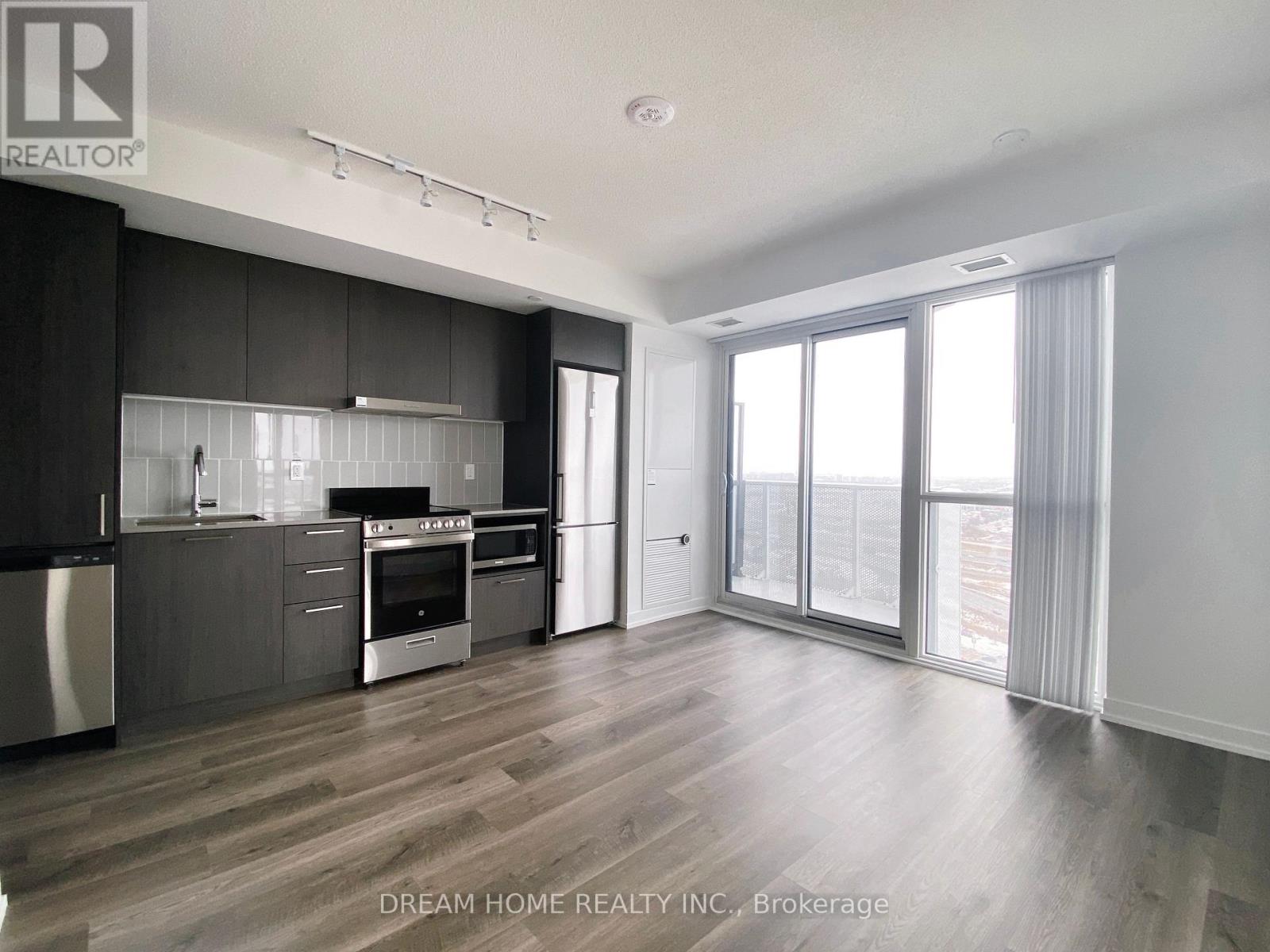 A modern kitchen with dark wood floors and stainless steel appliances.