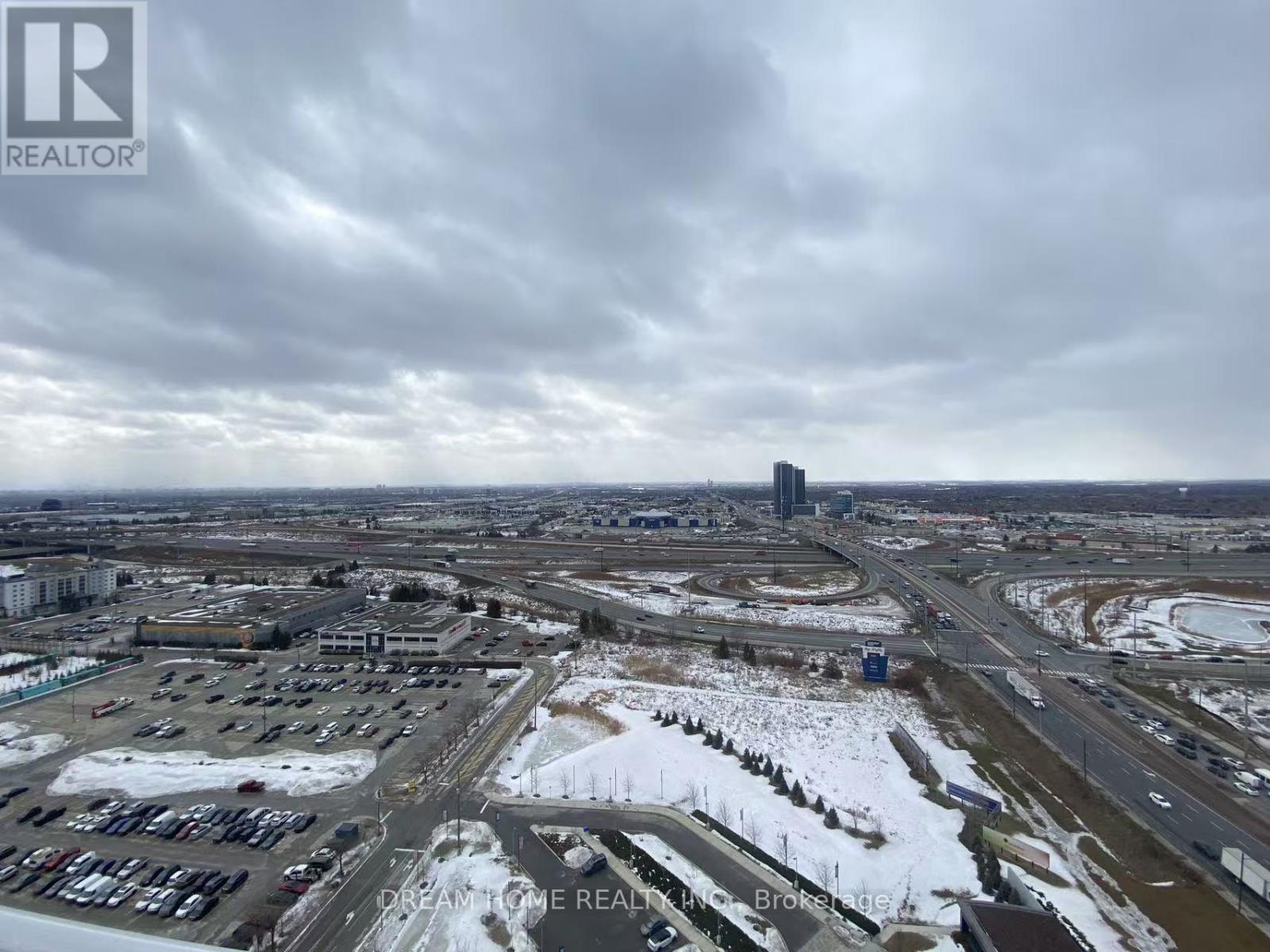 A real estate company logo is superimposed on a winter scene of a parking lot and buildings.