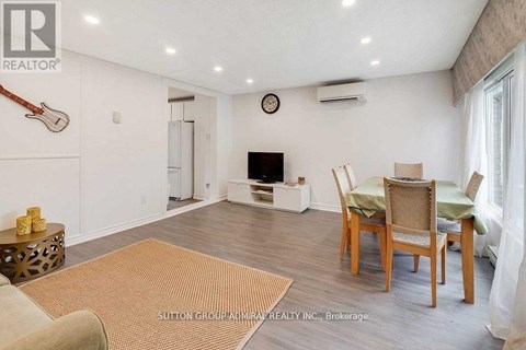 A living room with a brown rug, a wooden table with chairs, and a guitar hanging on the wall.