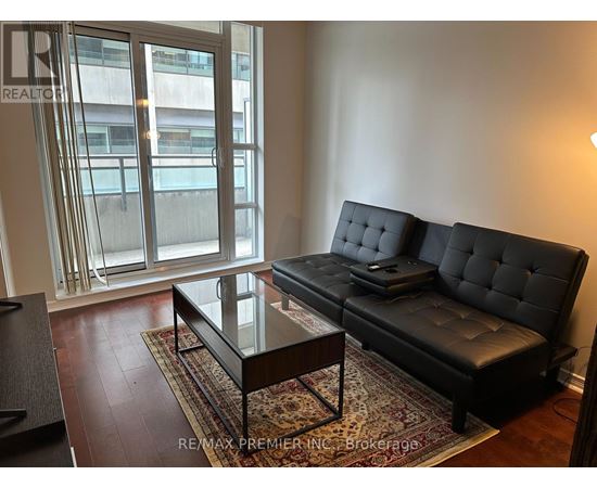 A black sofa with tufted detailing sits in a living room with a glass coffee table in front of it.