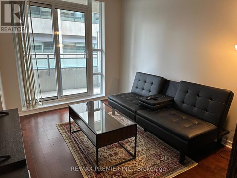 A black sofa with tufted detailing sits in a living room with a glass coffee table in front of it.