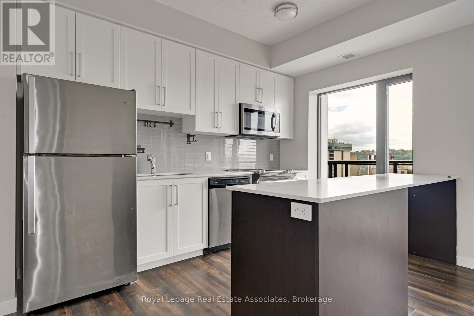 A modern kitchen with a stainless steel refrigerator and wooden floors.