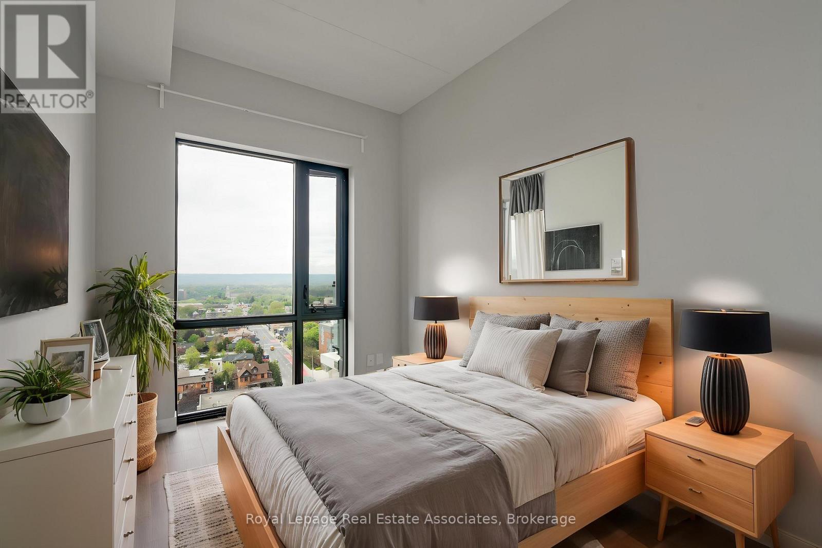 A bedroom with a large bed, a nightstand with a lamp, and a view of the city through the window.