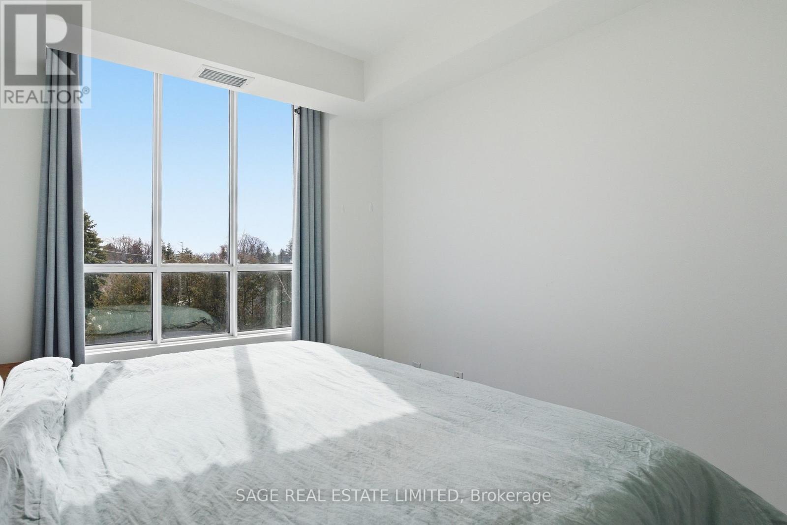 A bedroom with a large bed and a window overlooking a tree-filled landscape.