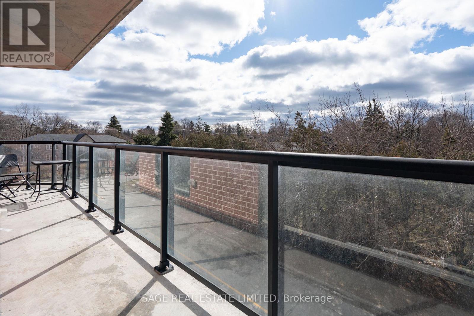 A balcony with a glass railing and a view of trees and sky.