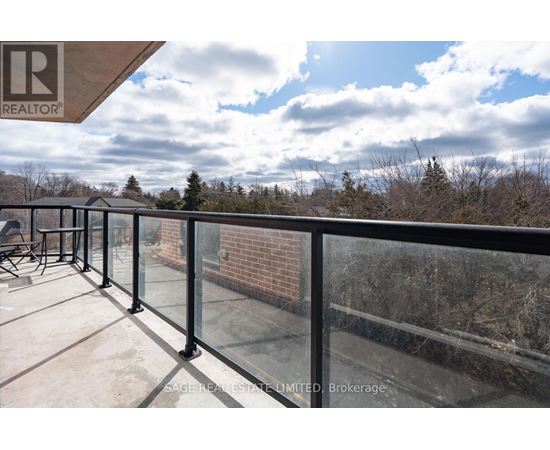 A balcony with a glass railing and a view of trees and sky.