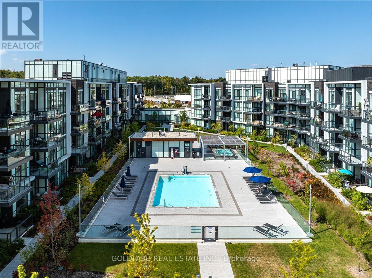 A swimming pool is surrounded by a grassy area and chairs in front of apartment buildings.