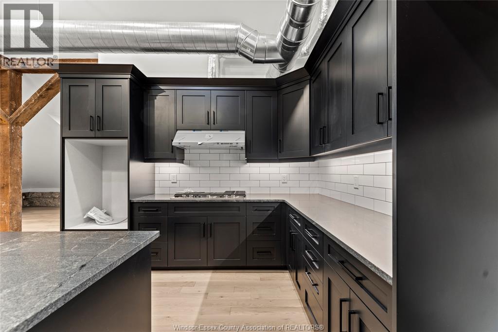 A modern kitchen with dark cabinets and a wooden staircase.