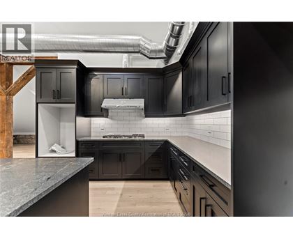 A modern kitchen with dark cabinets and a wooden staircase.