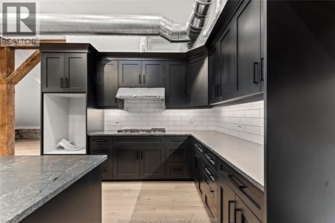 A modern kitchen with dark cabinets and a wooden staircase.