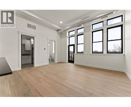 A spacious room with wooden flooring and large windows.