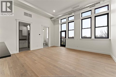 A spacious room with wooden flooring and large windows.