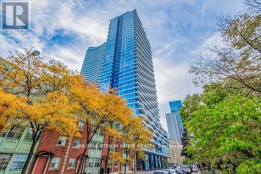 A tall blue building stands in front of a row of trees with autumn leaves.