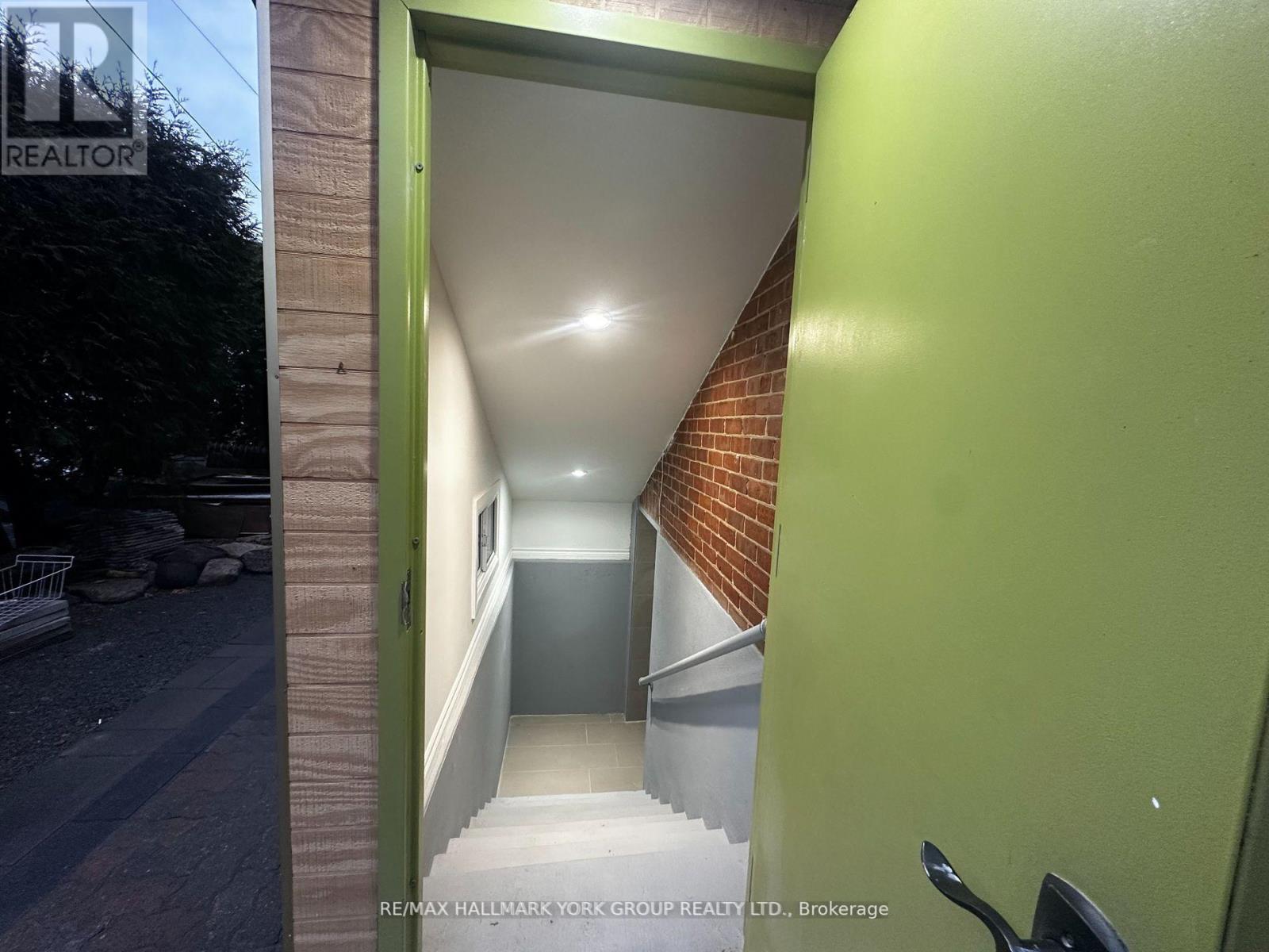A green doorway leads to a hallway with a brick wall on one side and a white wall on the other.
