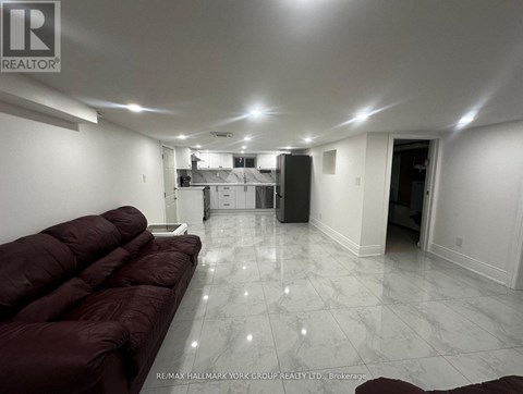 A spacious living room with a maroon sofa and a kitchen in the background.