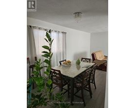 A dining room with a table set for two and a plant in the foreground.