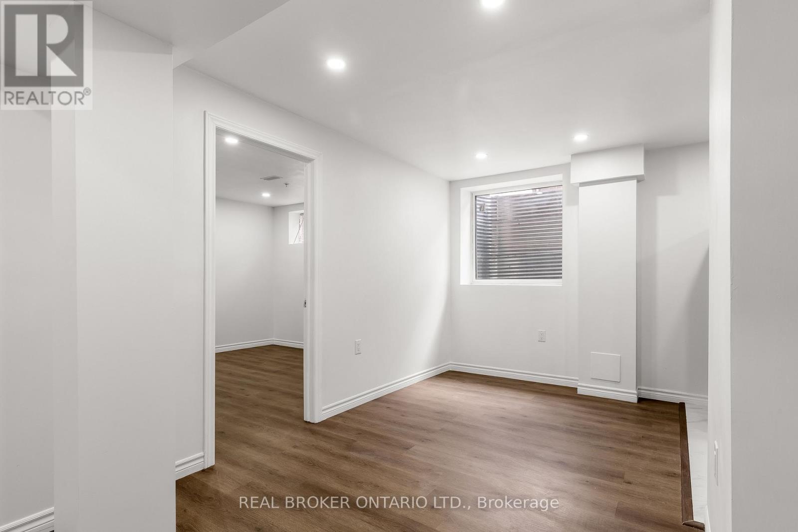 A white room with wood flooring and a window with blinds.