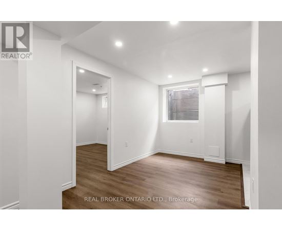 A white room with wood flooring and a window with blinds.