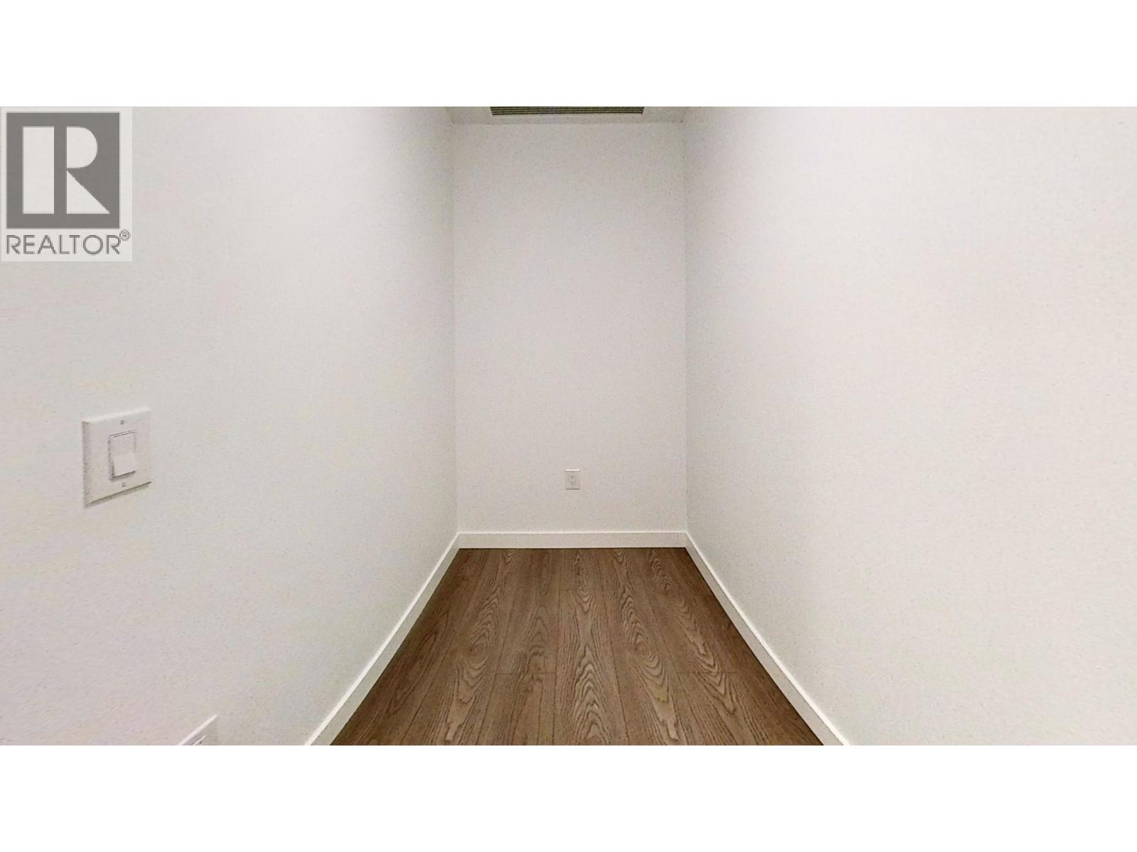 A white wall with a light switch and a wooden floor.