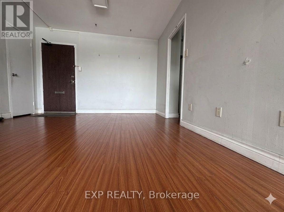 A room with wooden flooring and white walls, with a door on the left and a window on the right.
