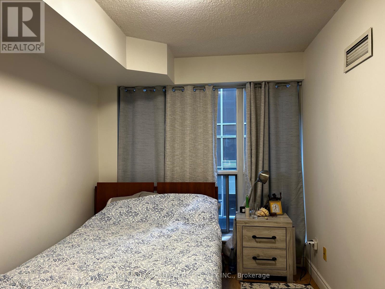 A bedroom with a bed, nightstand, and window with curtains.