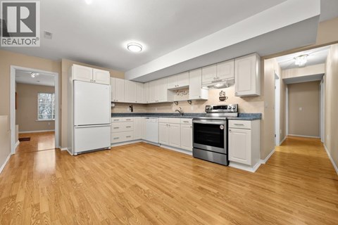 A well-lit, spacious kitchen with wooden floors and white appliances.