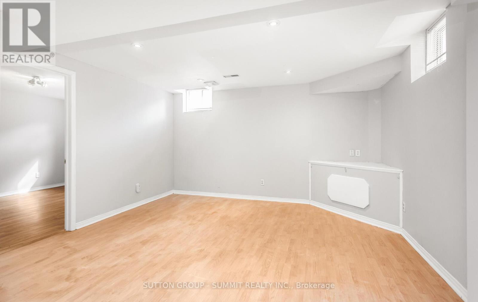 A room with wooden flooring and white walls, with a door on the left and a window on the right.