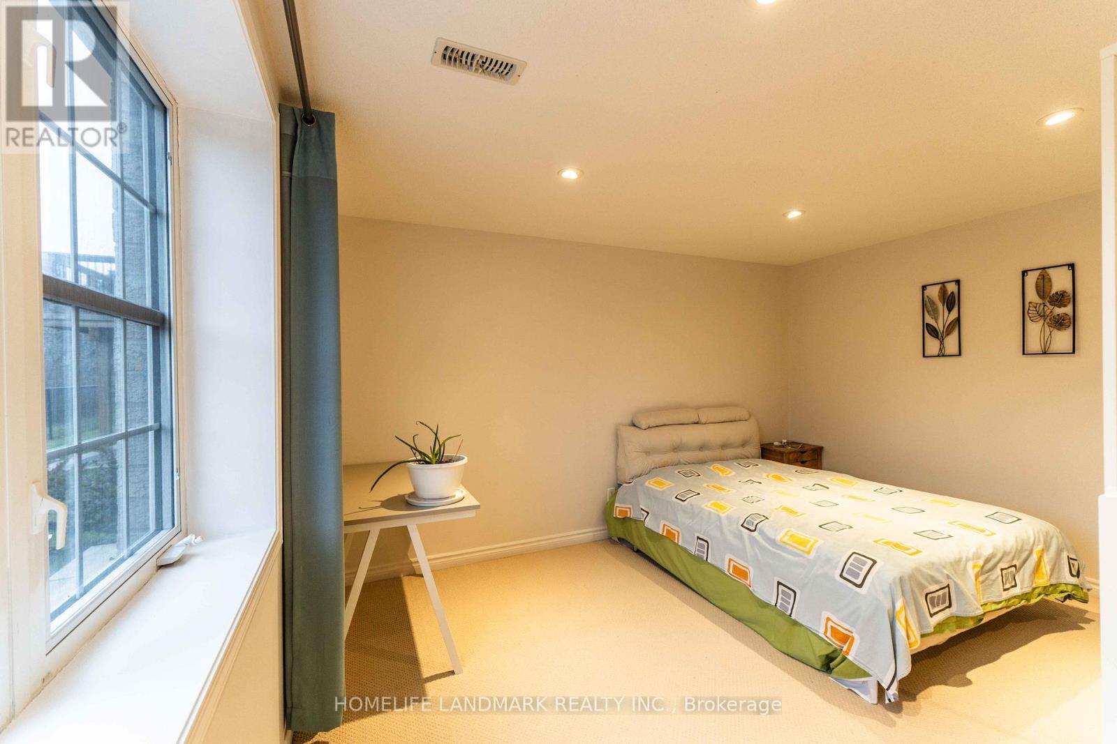 A bedroom with a bed, a small table with a plant, and a window with a view of a cityscape.