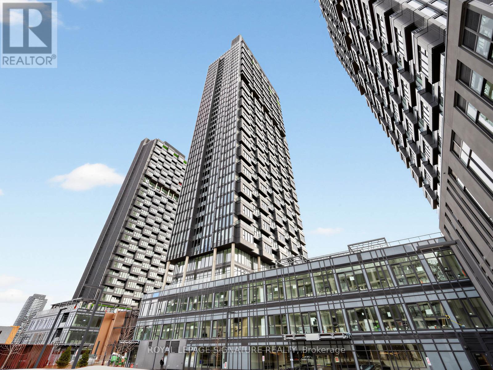 A tall building with a glass facade stands in front of other buildings.