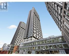 A tall building with a glass facade stands in front of other buildings.