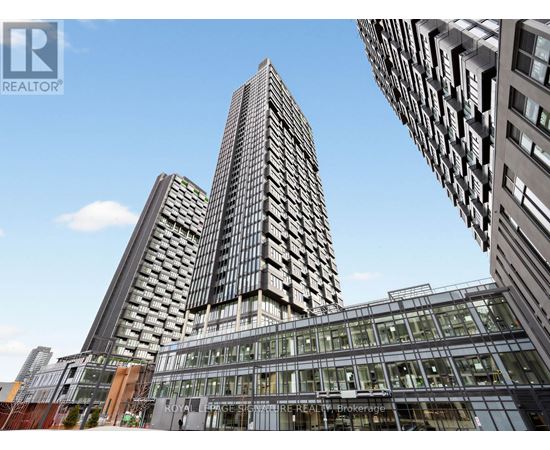 A tall building with a glass facade stands in front of other buildings.