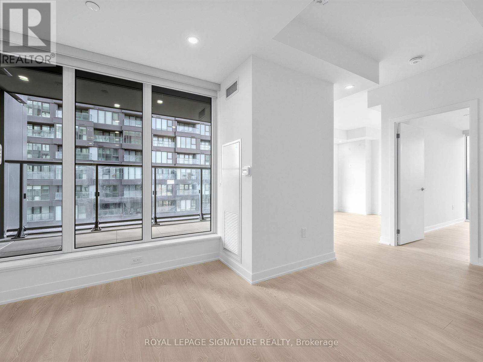 A spacious room with a large window overlooking a building and a doorway leading to another room.