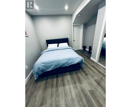 A bedroom with a bed, wooden flooring, and a mirror.