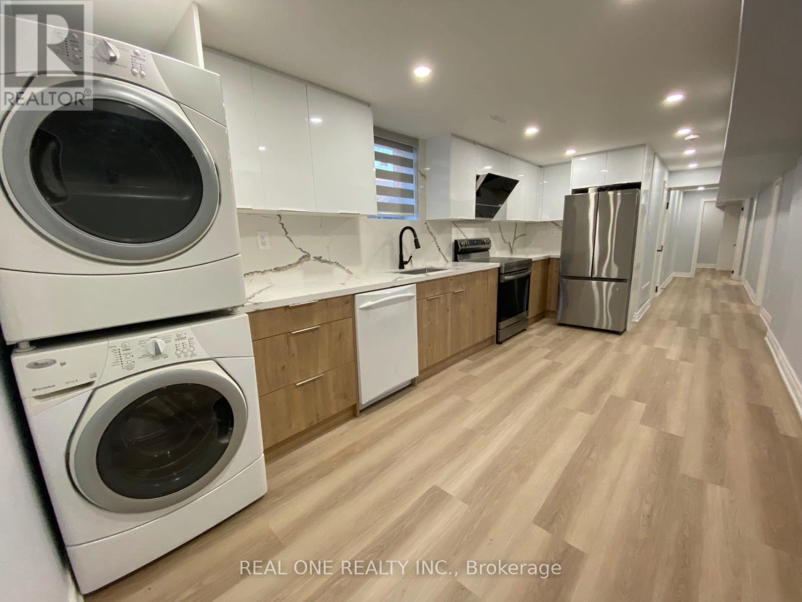 A real estate listing photo of a kitchen with white appliances and wood floors.