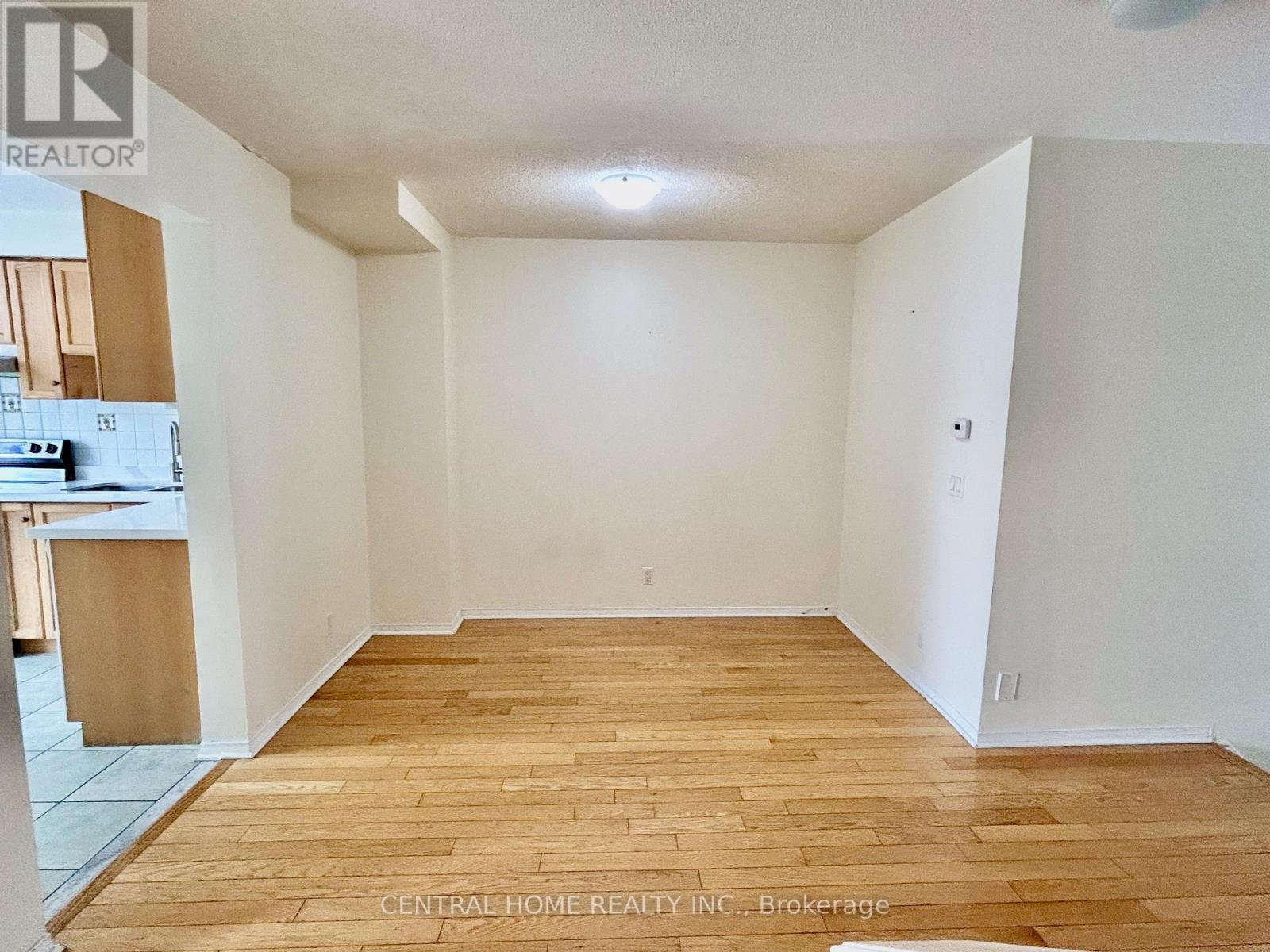 A room with wooden flooring and white walls, with a kitchen area visible in the background.