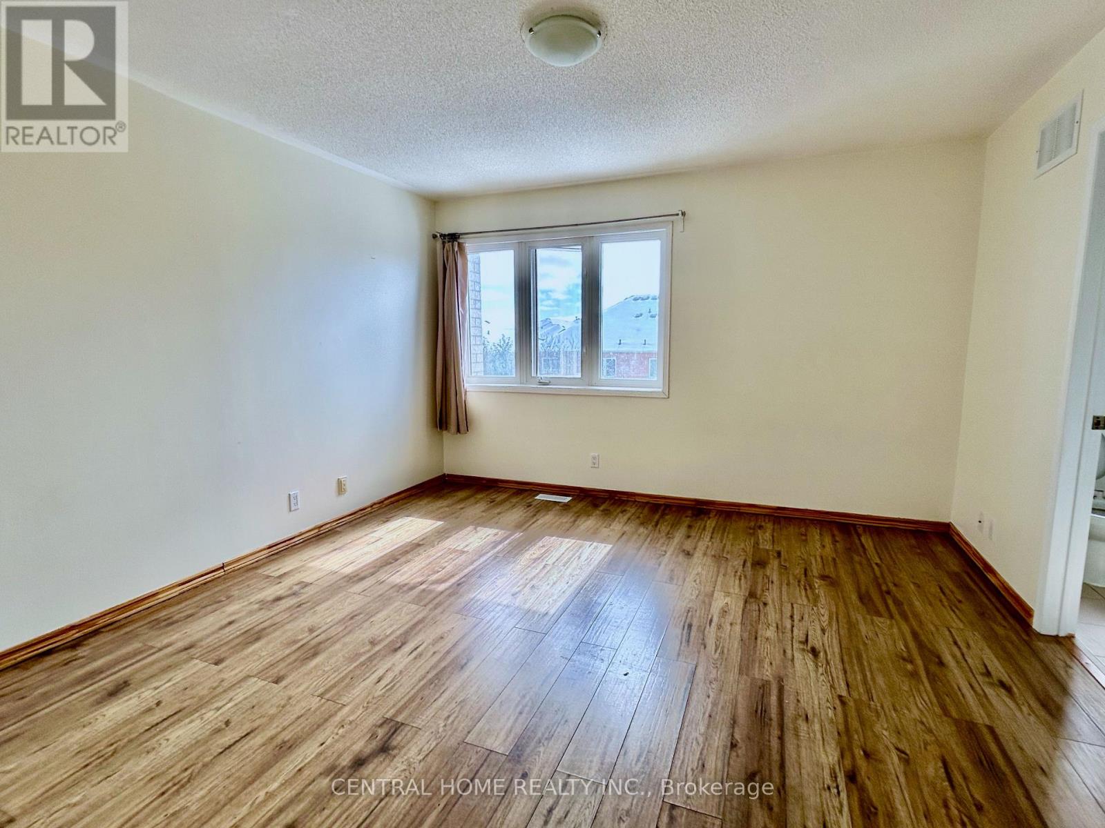 A room with wooden flooring and a window with a view of other buildings.