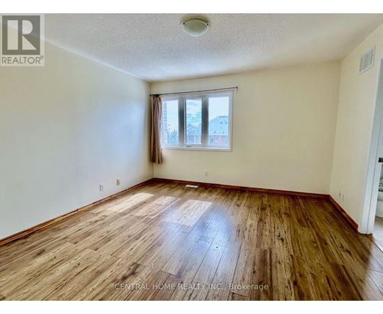 A room with wooden flooring and a window with a view of other buildings.