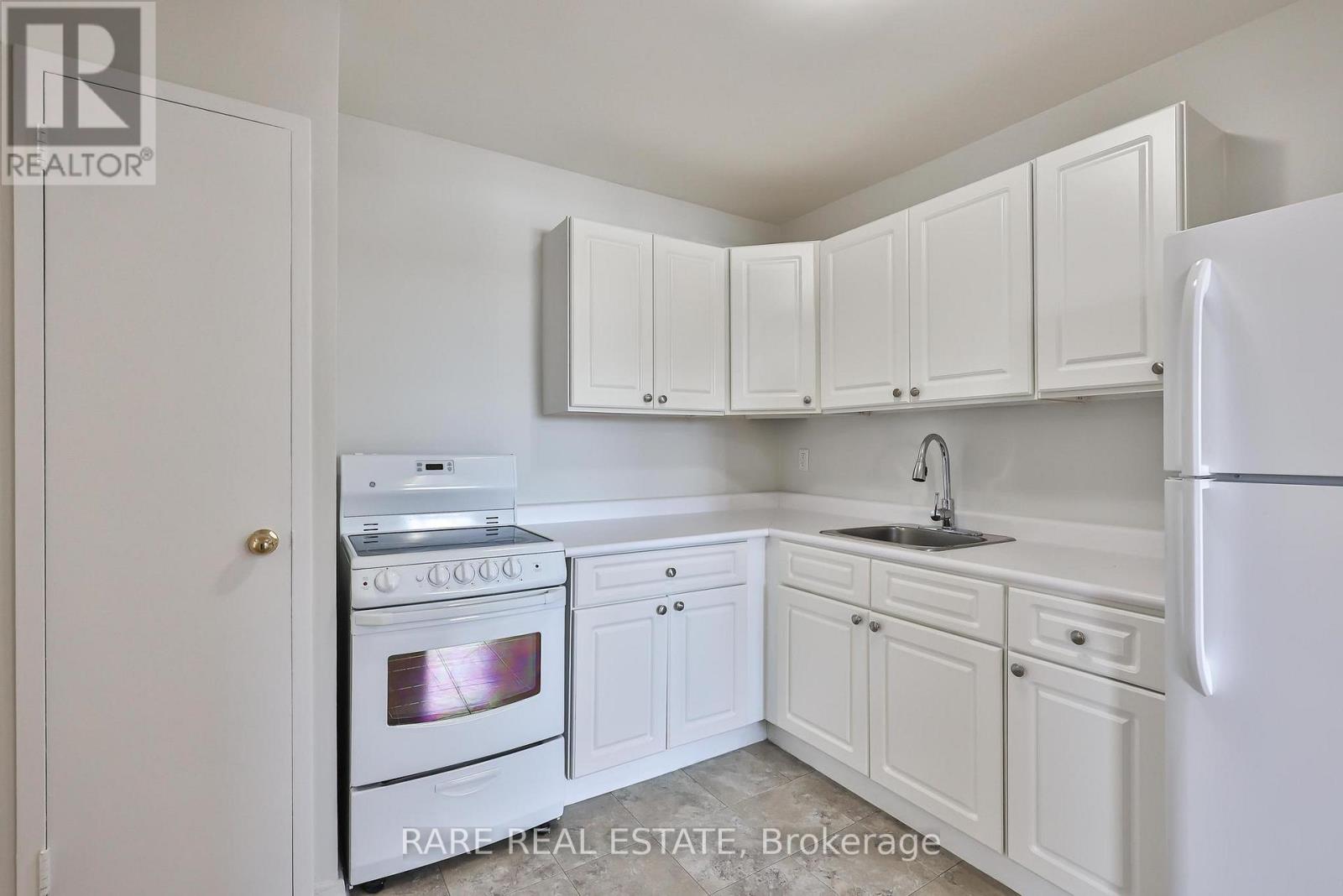 A white kitchen with a stove, sink, and cabinets.