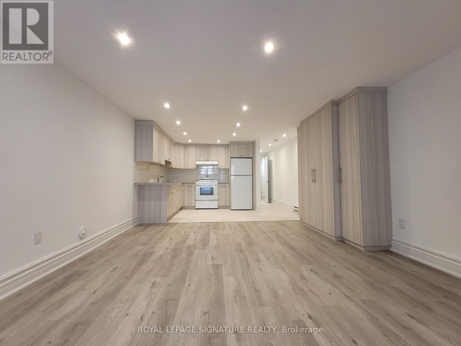 A spacious room with wooden flooring and a kitchen area with white appliances.