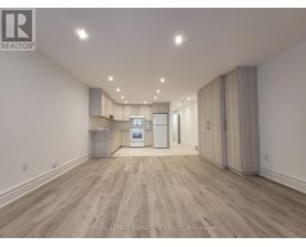 A spacious room with wooden flooring and a kitchen area with white appliances.