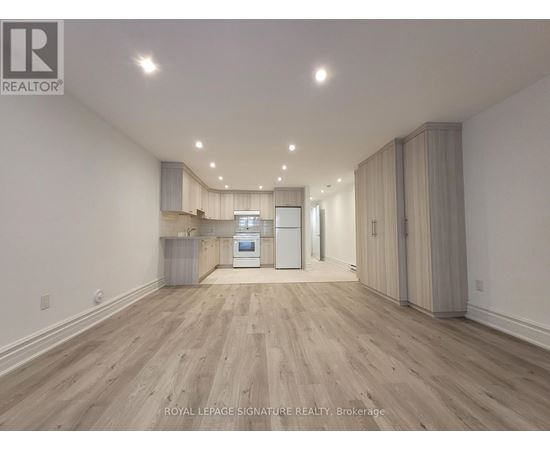 A spacious room with wooden flooring and a kitchen area with white appliances.