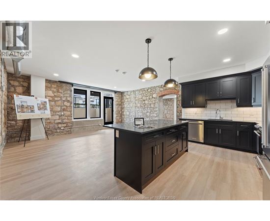 A kitchen with black cabinets and a stone wall.