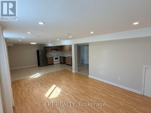 A spacious room with wooden flooring and a kitchen area in the background.
