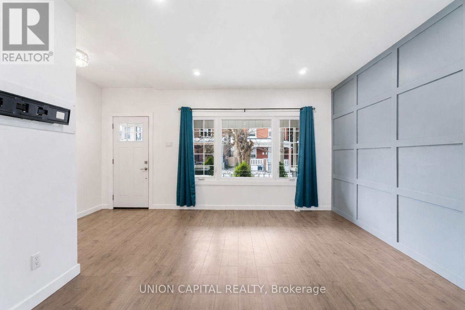 A spacious room with wooden flooring and a large window with curtains.
