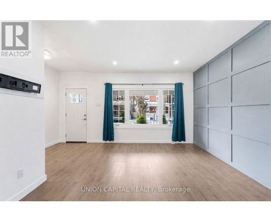 A spacious room with wooden flooring and a large window with curtains.