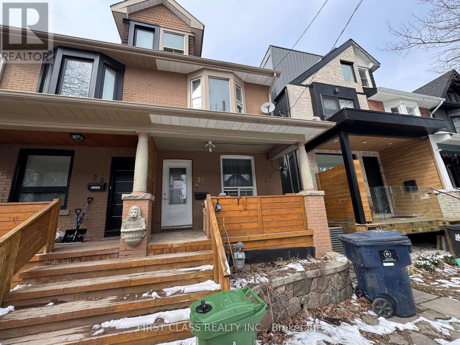 A house with a brown and beige exterior and a green trash can in front.